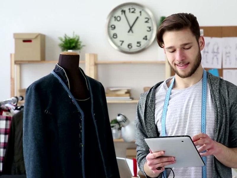 dizajner stoji pored svog rada koji visi na lutci i drži tablet u rukama